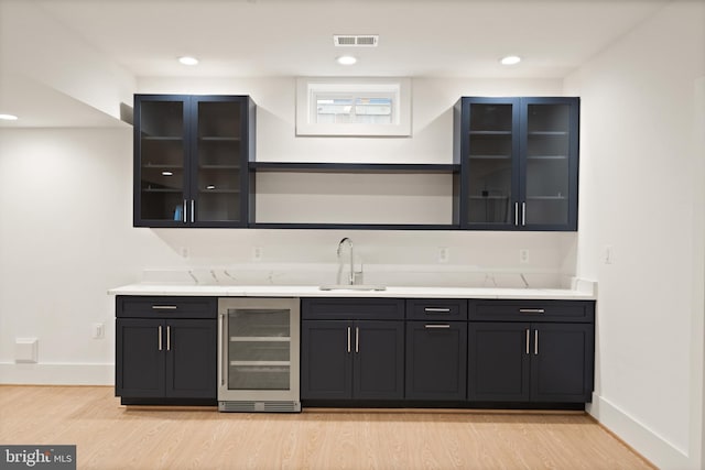 kitchen with visible vents, light wood-type flooring, a sink, wine cooler, and baseboards