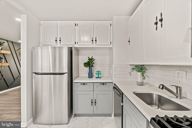 kitchen featuring a sink, decorative backsplash, light countertops, appliances with stainless steel finishes, and marble finish floor