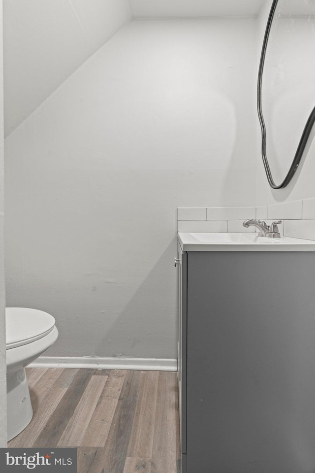 half bathroom with vanity, lofted ceiling, toilet, and wood finished floors