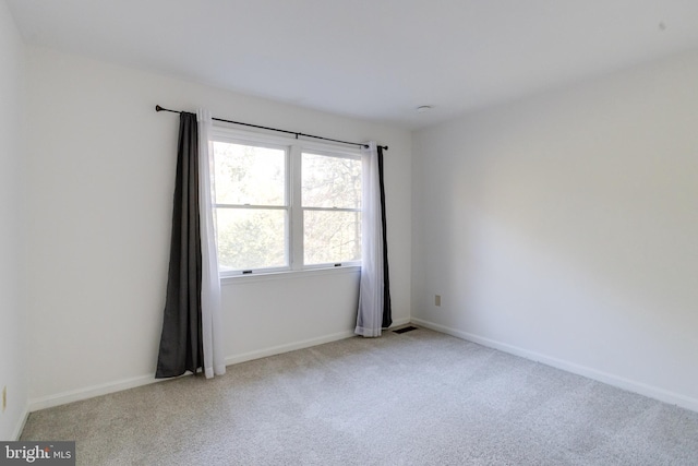 empty room featuring visible vents, light colored carpet, and baseboards