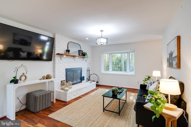 living area with baseboards, a brick fireplace, and wood finished floors