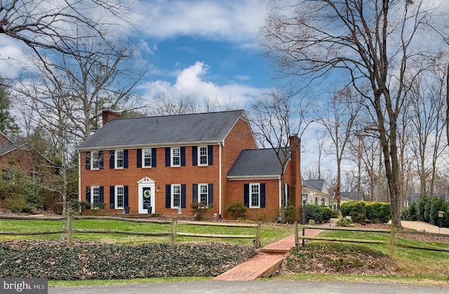 view of front of house with a fenced front yard, a front yard, brick siding, and a chimney