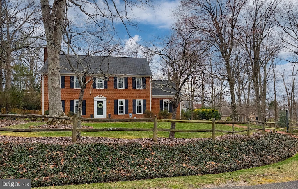 colonial house featuring brick siding, a chimney, a front yard, and fence