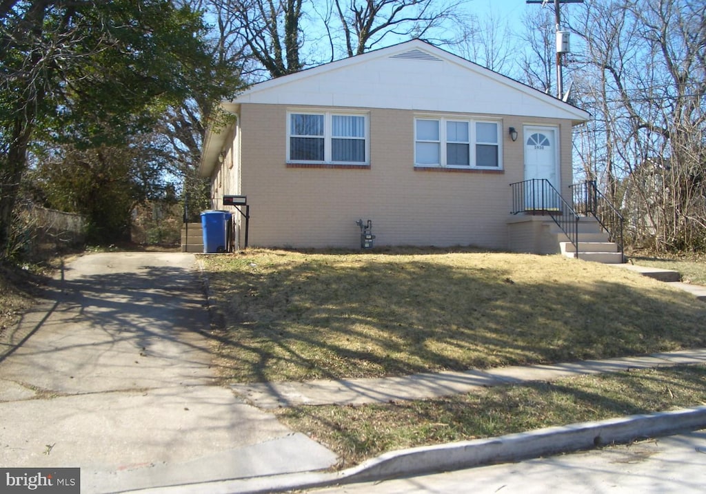 view of front of house featuring brick siding, concrete driveway, and a front yard