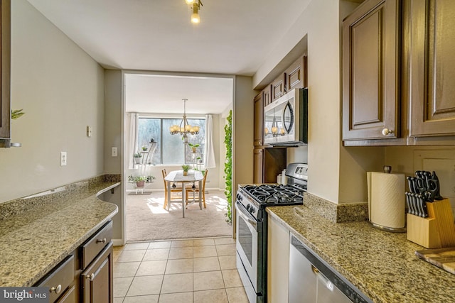 kitchen featuring light tile patterned floors, light stone countertops, an inviting chandelier, stainless steel appliances, and light colored carpet