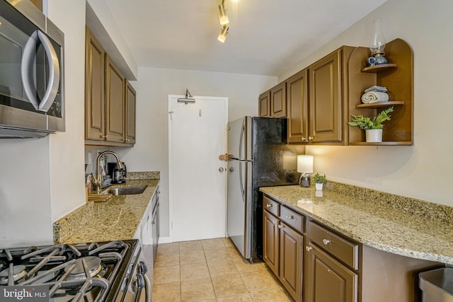 kitchen with a sink, open shelves, appliances with stainless steel finishes, light tile patterned flooring, and light stone countertops