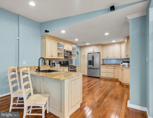 kitchen with a sink, cream cabinets, hardwood / wood-style floors, stainless steel appliances, and a peninsula