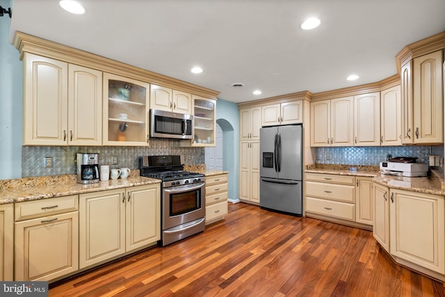 kitchen with cream cabinetry, arched walkways, appliances with stainless steel finishes, and dark wood-type flooring