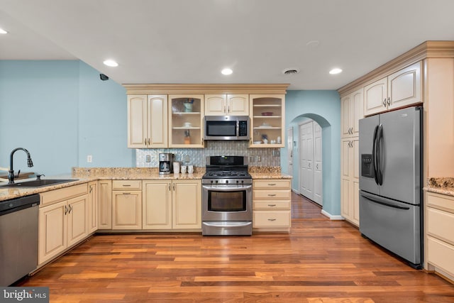 kitchen with a sink, stainless steel appliances, backsplash, and cream cabinetry