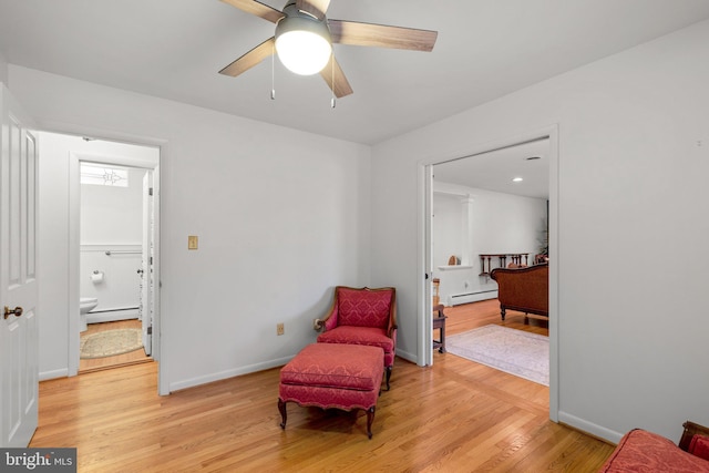 sitting room with a baseboard heating unit, baseboards, baseboard heating, and light wood-style flooring