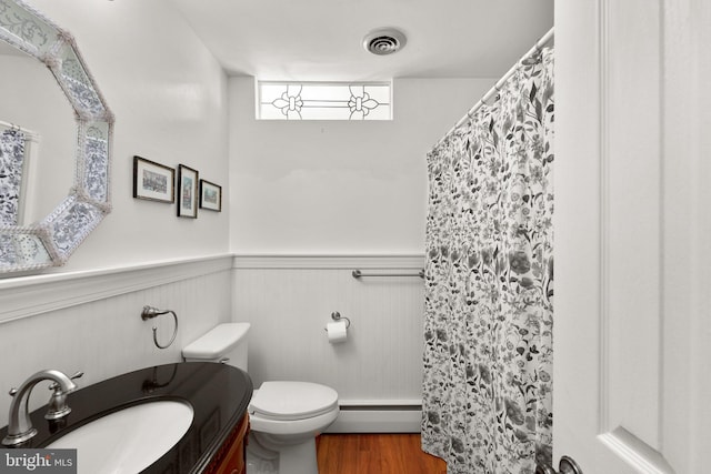 bathroom with visible vents, toilet, wood finished floors, wainscoting, and baseboard heating