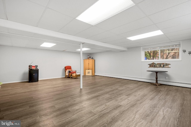 basement featuring a drop ceiling, baseboards, wood finished floors, and a baseboard heating unit