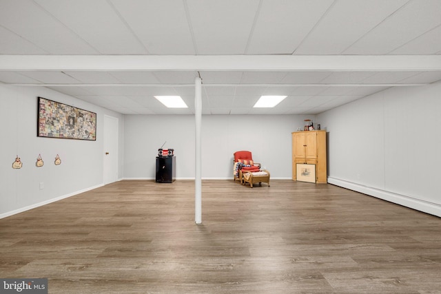 finished below grade area featuring a baseboard radiator, a paneled ceiling, baseboards, and wood finished floors