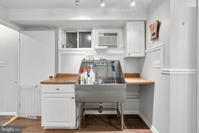 kitchen featuring a wall mounted air conditioner, wood finished floors, white cabinets, glass insert cabinets, and baseboards