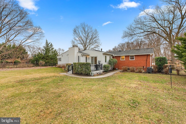 rear view of property with a yard, brick siding, central AC, and a chimney