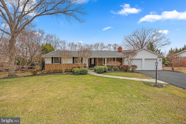 ranch-style house featuring brick siding, an attached garage, a front lawn, a chimney, and driveway