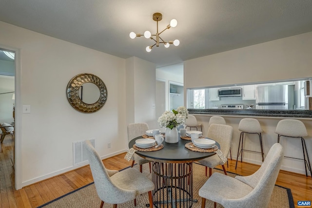 dining area with visible vents, baseboards, light wood-style floors, and an inviting chandelier