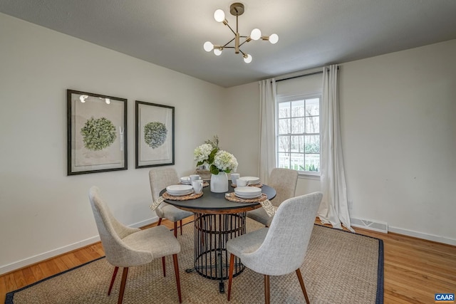 dining area featuring a chandelier, visible vents, baseboards, and wood finished floors