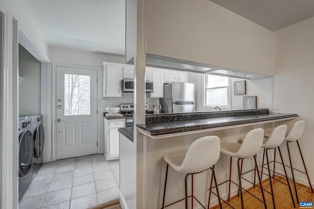 kitchen featuring washing machine and clothes dryer, dark countertops, a breakfast bar, appliances with stainless steel finishes, and white cabinets