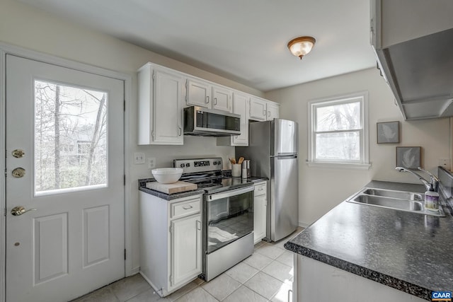 kitchen featuring a sink, dark countertops, appliances with stainless steel finishes, white cabinets, and light tile patterned floors