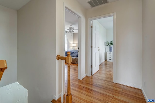 hall with an upstairs landing, visible vents, light wood-type flooring, and baseboards