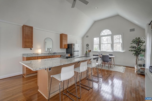 kitchen featuring wood-type flooring, a breakfast bar, brown cabinetry, and freestanding refrigerator