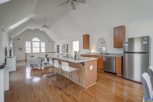 kitchen with a kitchen island, a breakfast bar, brown cabinets, stainless steel appliances, and open floor plan