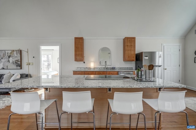 kitchen featuring a spacious island, appliances with stainless steel finishes, wood finished floors, brown cabinetry, and a sink