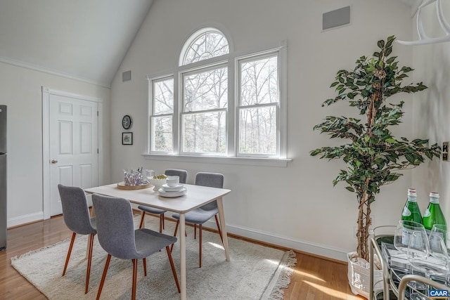 dining space with visible vents, baseboards, wood finished floors, and vaulted ceiling