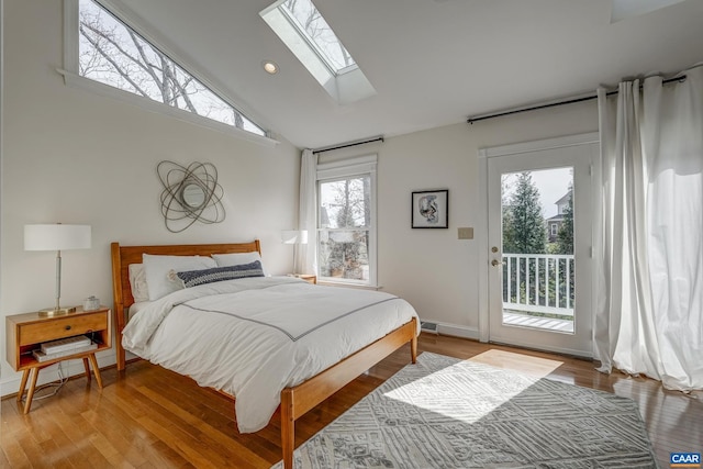 bedroom featuring baseboards, a skylight, wood finished floors, high vaulted ceiling, and access to outside