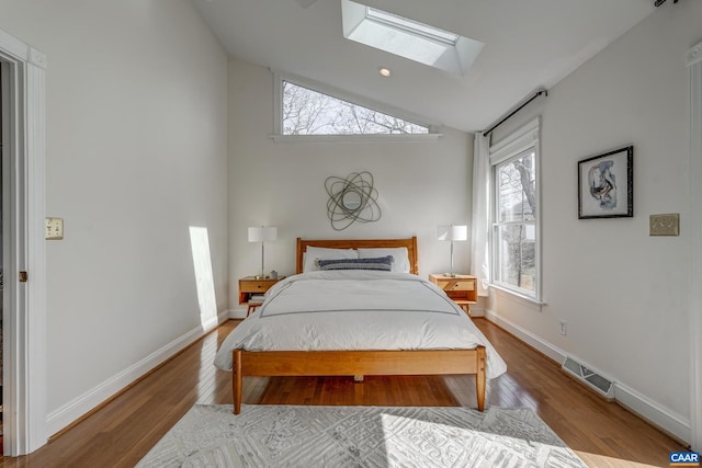 bedroom with lofted ceiling with skylight, wood finished floors, visible vents, and baseboards