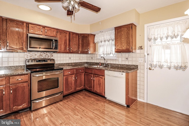 kitchen featuring light wood-style flooring, ceiling fan, a sink, appliances with stainless steel finishes, and dark countertops