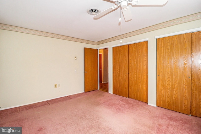 unfurnished bedroom with visible vents, ceiling fan, carpet, multiple closets, and ornamental molding