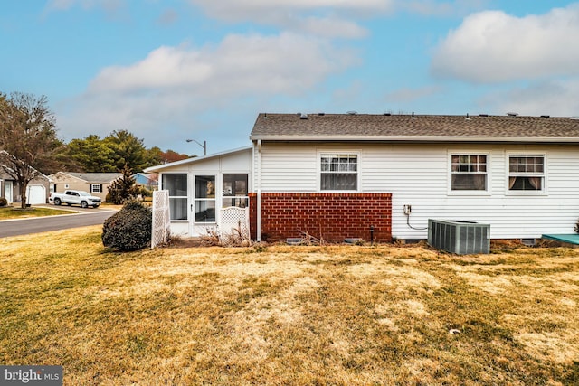 exterior space featuring central AC unit, a lawn, a sunroom, and roof with shingles