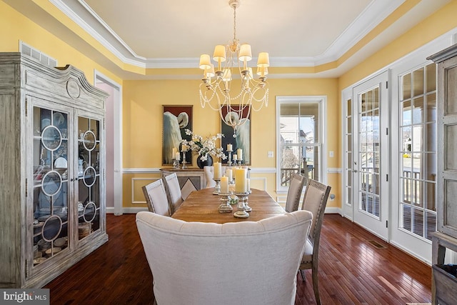 dining area with an inviting chandelier, french doors, dark wood-type flooring, and a tray ceiling