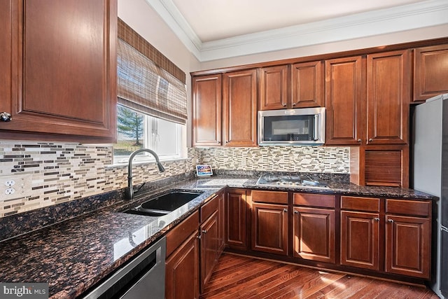 kitchen with dark stone counters, a sink, ornamental molding, dark wood-type flooring, and stainless steel appliances