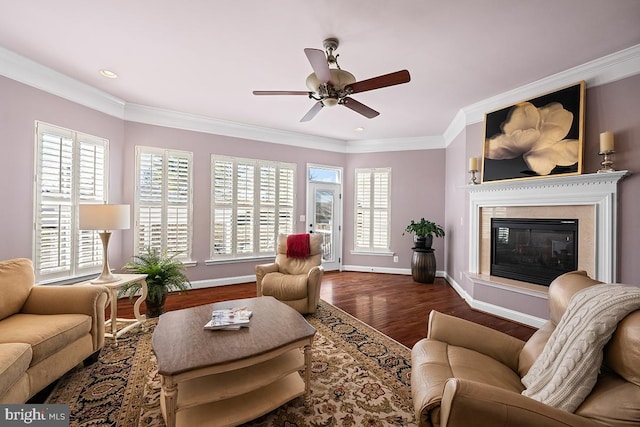 living room featuring wood finished floors, a glass covered fireplace, crown molding, baseboards, and ceiling fan