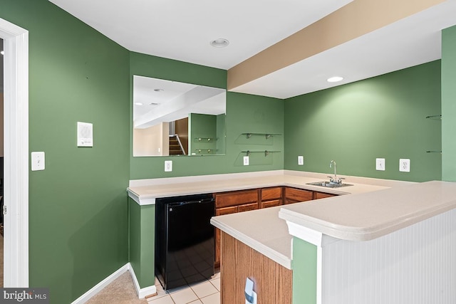 kitchen with light countertops, light tile patterned floors, a peninsula, fridge, and a sink