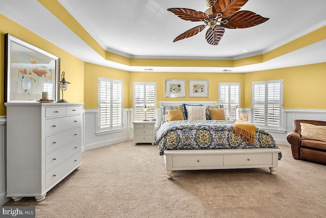 carpeted bedroom featuring a tray ceiling, multiple windows, crown molding, and a wainscoted wall