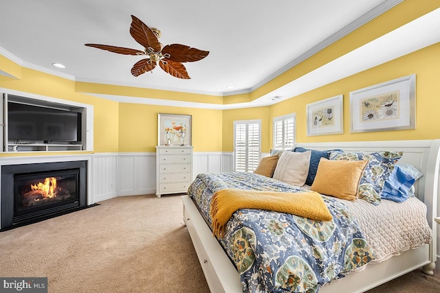 carpeted bedroom featuring a ceiling fan, a wainscoted wall, a fireplace with flush hearth, recessed lighting, and crown molding