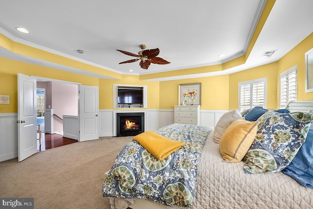 bedroom with visible vents, a lit fireplace, wainscoting, crown molding, and carpet flooring