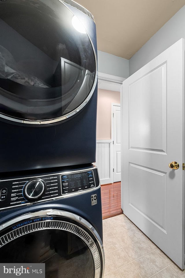 laundry area with a wainscoted wall, laundry area, light tile patterned floors, and stacked washer and clothes dryer