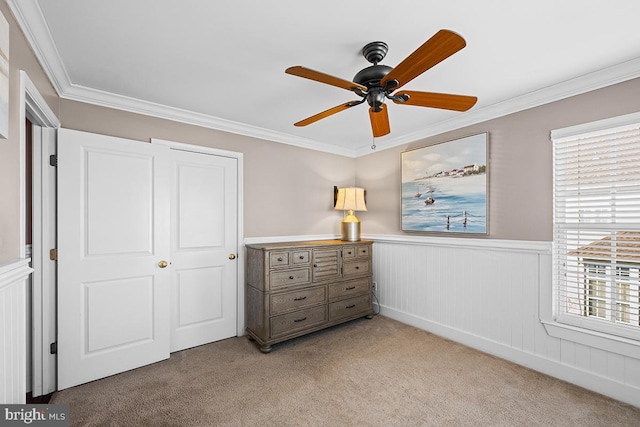 bedroom with ceiling fan, light colored carpet, ornamental molding, and wainscoting