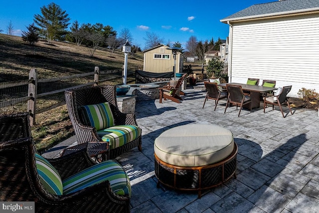 view of patio / terrace with an outbuilding, fence, a shed, an outdoor living space with a fire pit, and outdoor dining area