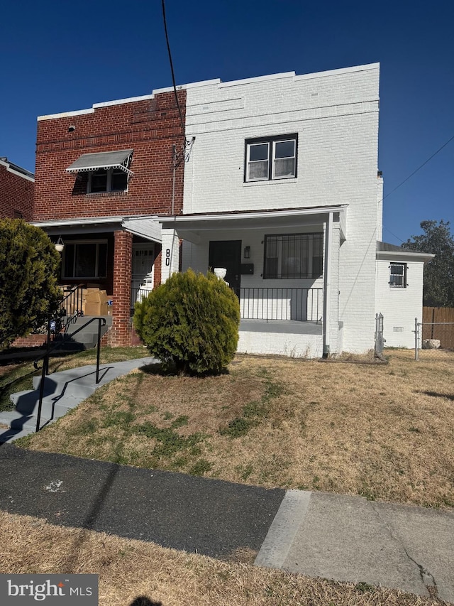 view of property featuring brick siding, covered porch, and a front lawn