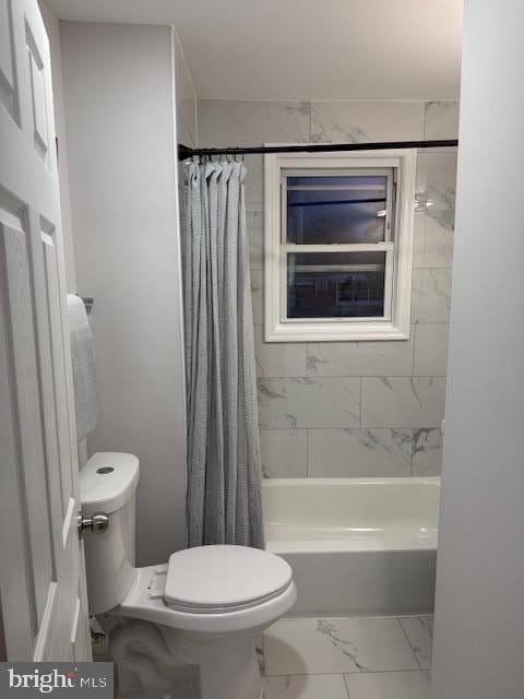 full bath with toilet, marble finish floor, and shower / tub combo with curtain