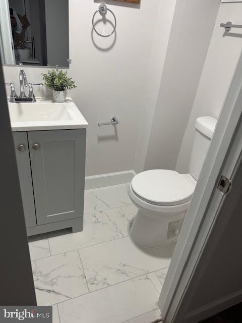 half bathroom with baseboards, marble finish floor, vanity, and toilet