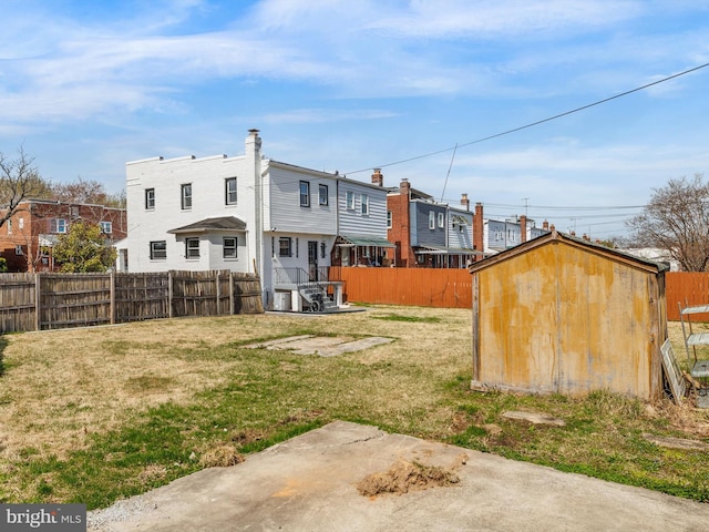 rear view of house with a storage unit, a yard, an outbuilding, and a fenced backyard