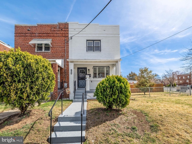 view of front of home with brick siding, covered porch, a front lawn, and fence