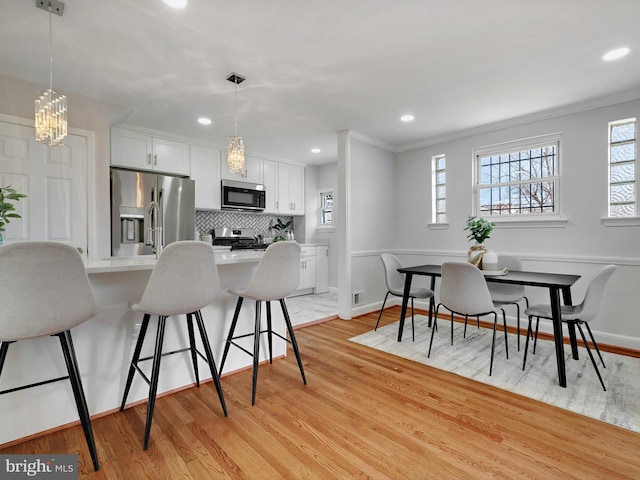 kitchen featuring light wood-style flooring, a kitchen breakfast bar, tasteful backsplash, white cabinetry, and appliances with stainless steel finishes